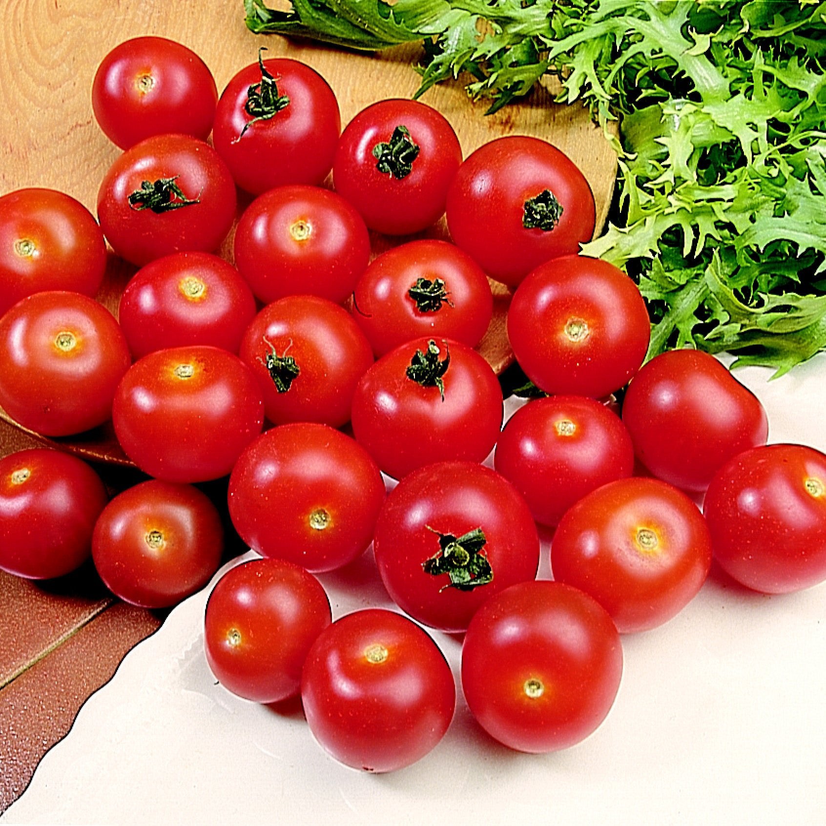 A pile of bright red cherry tomatoes harvested from Tomato Plants Gardeners Delight, arranged on a surface with fresh green salad leaves nearby