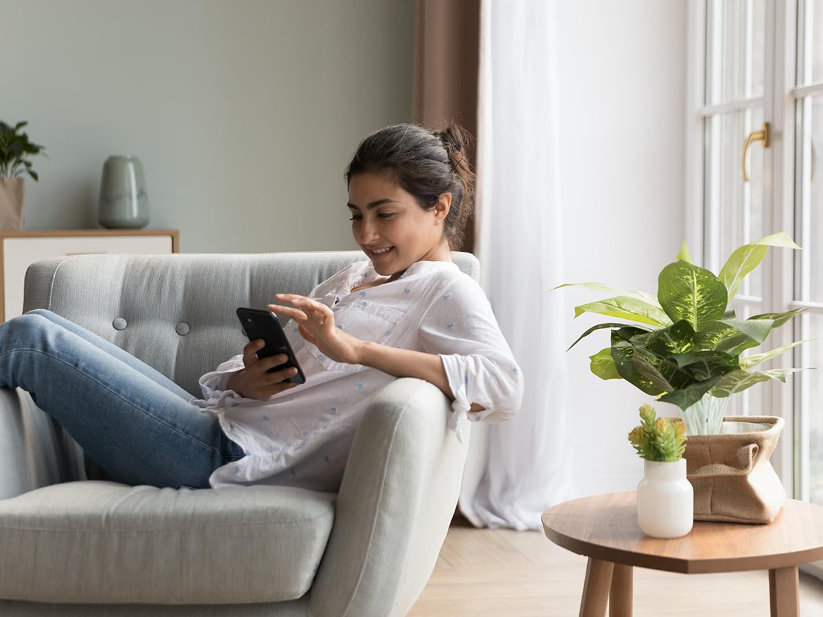 low maintenance indoor plants Woman sitting on a couch using a smartphone in a bright living room.